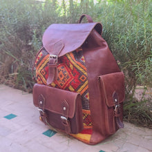 Load image into Gallery viewer, Brown leather backpack with colorful pattern on a stone path