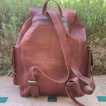 Load image into Gallery viewer, Brown leather backpack on a stone surface with greenery in the background