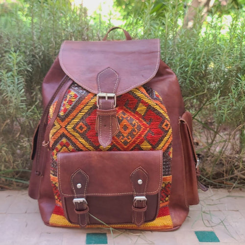 Brown leather backpack with colorful pattern on a stone surface with greenery in the background